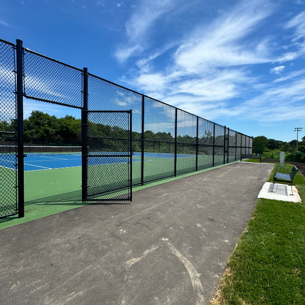 Fenced tennis courts with a gate and bench.
