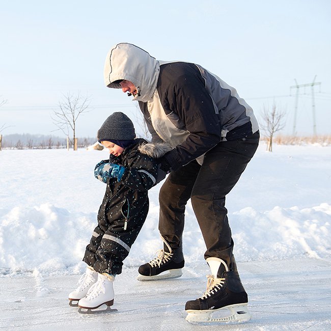 Grandfather teaching grandchild how to skate on an outdoor rink.