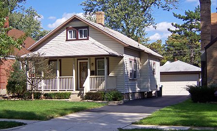 The front yard of a small home showing the yard, driveway, sidewalk and boulevard