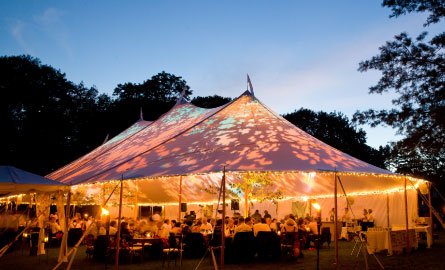 pecial event tent lit up from the inside with dark blue night time sky and trees