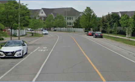 A straight two-lane road in a rural area with white and yellow lines to guide traffic.