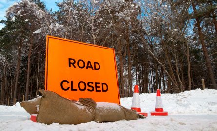 A road closure sign blocking the way on a snowy street.